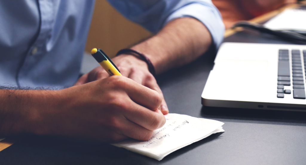 A man taking notes by his laptop during a field interview