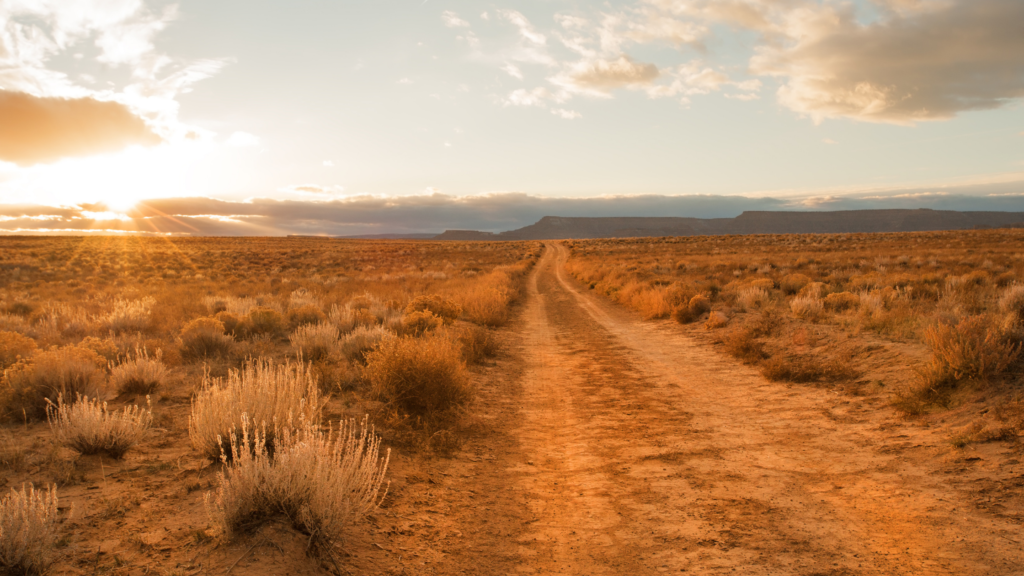 Dirt road through desert with mountains and sunset in the background